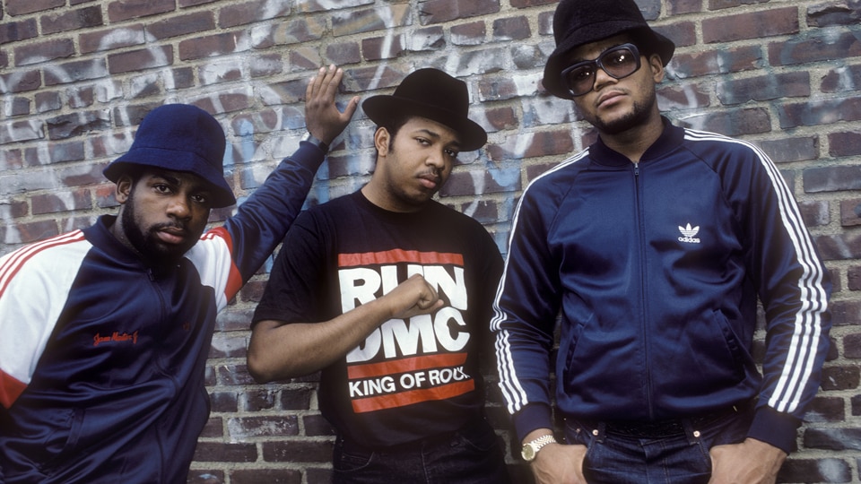 Hip-hop group Run-D.M.C. (Joseph Simmons, Darryl McDaniels, and Jason Mizell) posing against a brick wall, circa 1985.