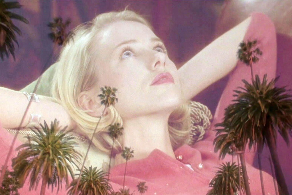 A blond woman (played by Naomi Watts) lies on her back, looking upward, as palm trees are superimposed over her.