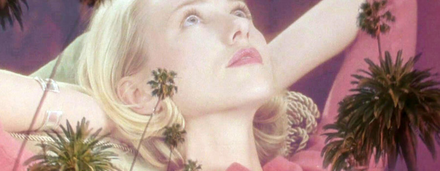 A blond woman (played by Naomi Watts) lies on her back, looking upward, as palm trees are superimposed over her.