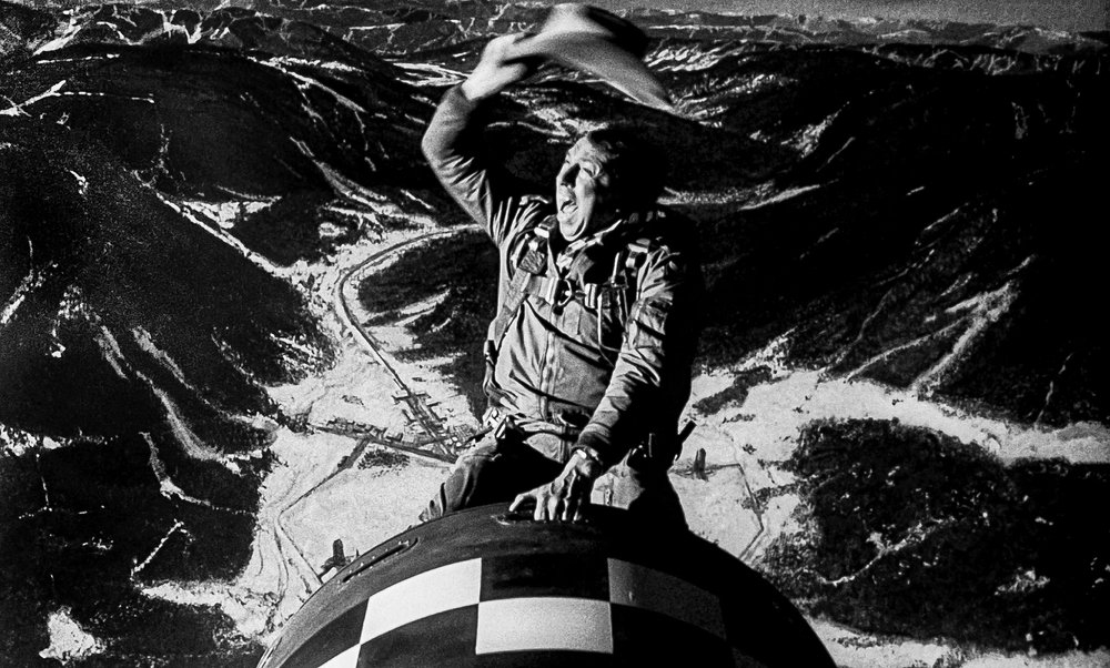 A black-and-white photo of a cowboy riding a missile as it descends to earth.