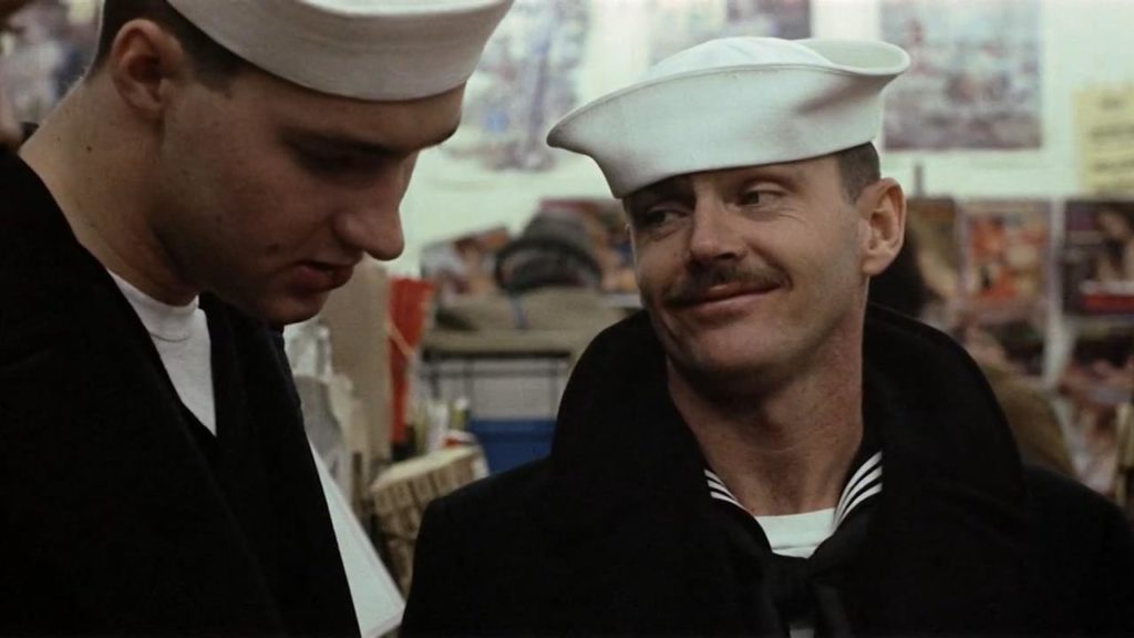 A Navy officer looks at another sailor in a store, offering a smirk.