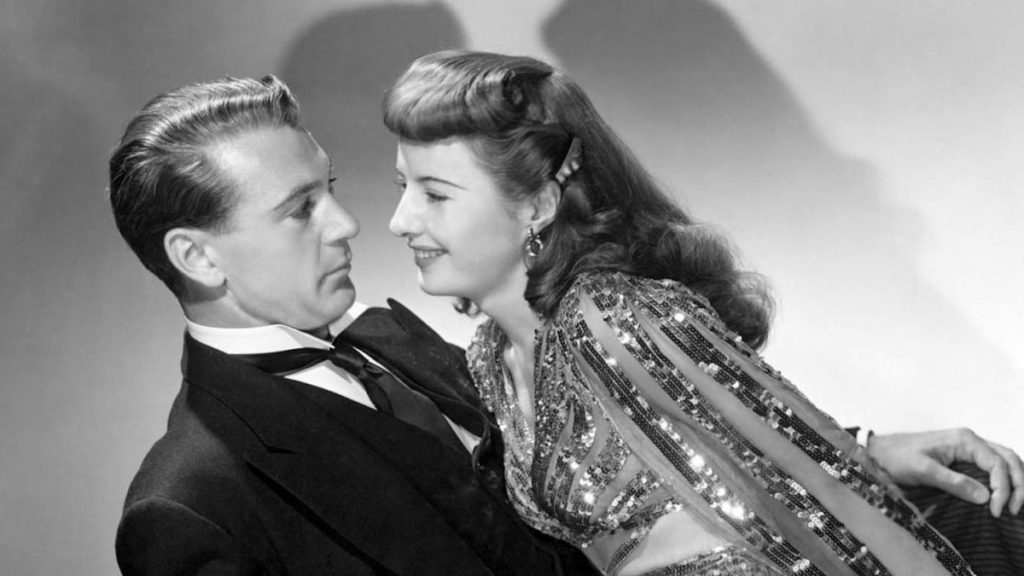 A black-and-white image of a woman in a sequined dress (Barbara Stanwyck) leaning against a man in a tuxedo (Gary Cooper). 