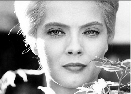 A black-and-white image of a woman holding a flower looking enigmatically at the camera.