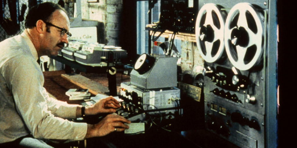 A bespectacled technician played by Gene Hackman operates sound recording equipment.