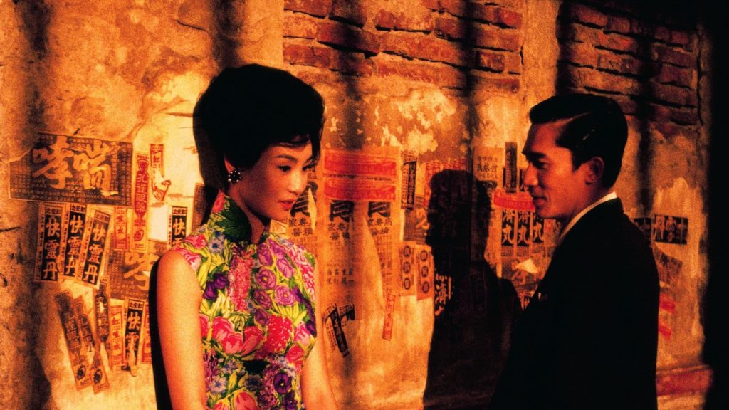 In an alley illuminated by golden light, a man in a suit looks at a woman wearing a bright, floral dress.