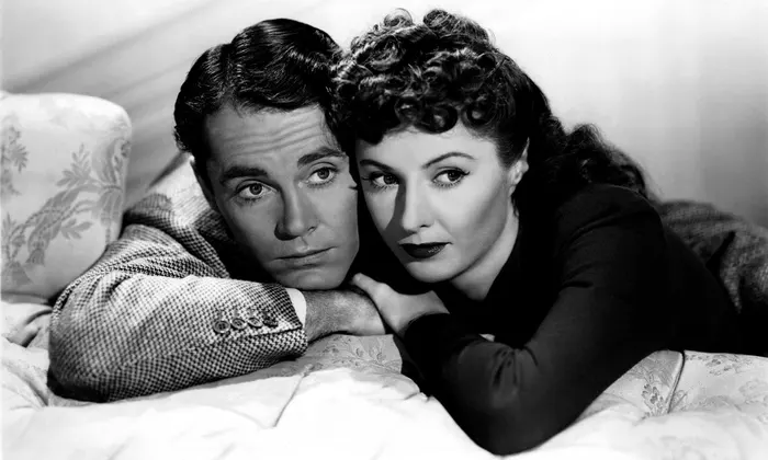 A black-and-white image of a man (Henry Fonda) and woman (Barbara Stanwyck) leaning on a bed, their heads resting on their hands.
