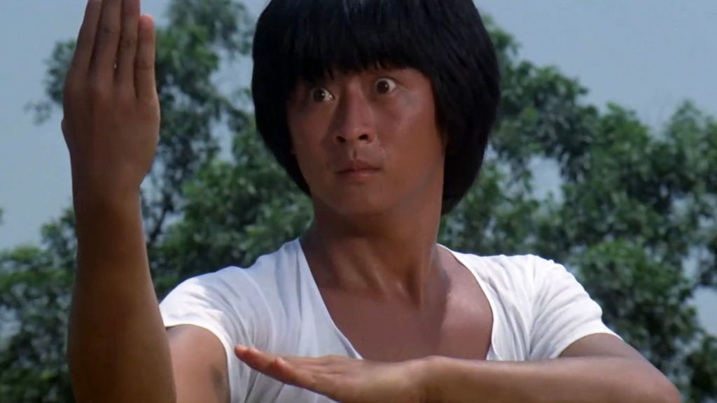 Yi-Min Li as Hsa Haio-ying in "7 Grandmasters," wearing a white shirt and striking a martial arts pose with a surprised expression on his face. 