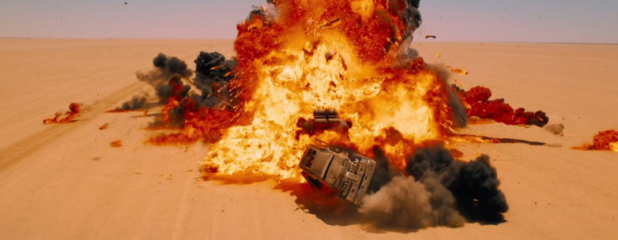 A large, fiery explosion erupts in the center of the desert. There is a large vehicle inside it, and a car flying toward the viewer. Behind it, smoke billows toward the sky.