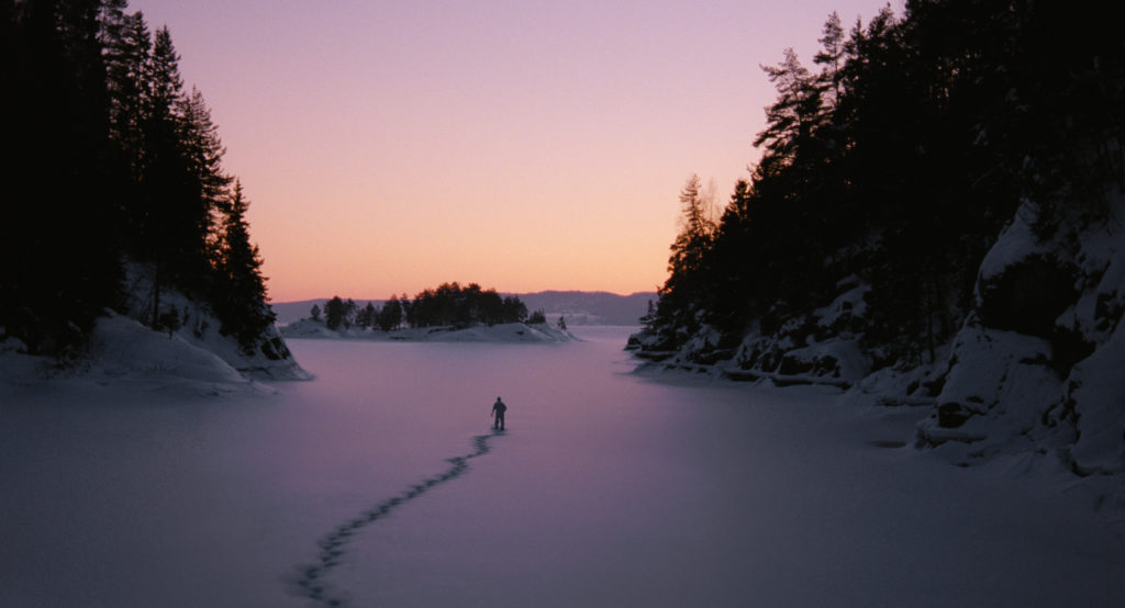 A lone human figure wanders through a wintry landscape. Shot from the film Essential Killing. 