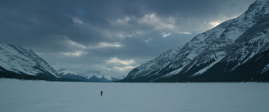 A lone human figure wanders through a wintry landscape. Shot from the film The Revenant.