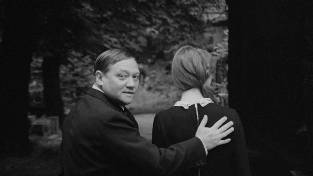 A man, Karel, places his hand on the back of a woman in the film "The Cremator."