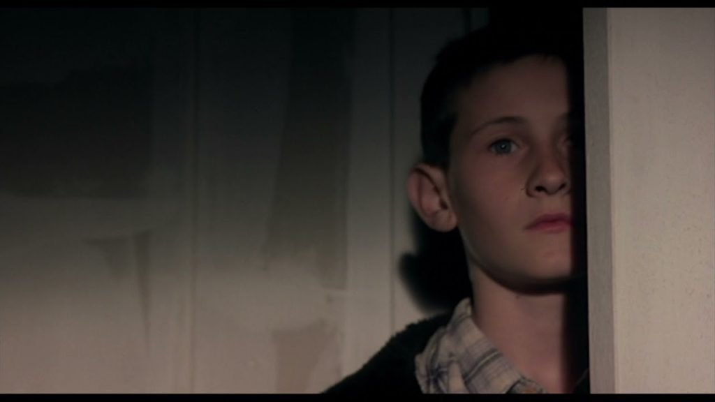 Jamie, a teenager living in 1970s Scotland, looks around a corner, half in shadow, in the movie "Ratcatcher."