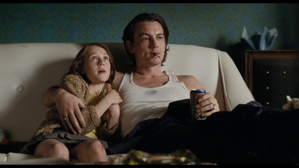 A standout performance in the film is that of Tommy Flanagan (right). Flanagan plays George, the hard drinking patriarch that is celebrated with a brief moment of heroism in the film. Here, he sits on a couch with his arm around his daughter; he cigarette and holds a can of something in his left hand. 