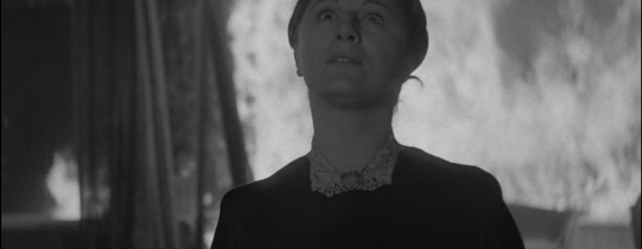 Judith Anderson looks to the heavens with an expression of fear and awe while a bedroom burns around her in the film Rebecca.