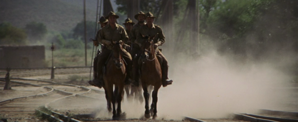 The Wild Bunch riding horses into town on a dusty trail. 