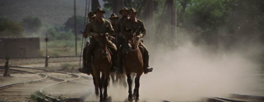 The Wild Bunch rides into town on a dusty trail on horseback.