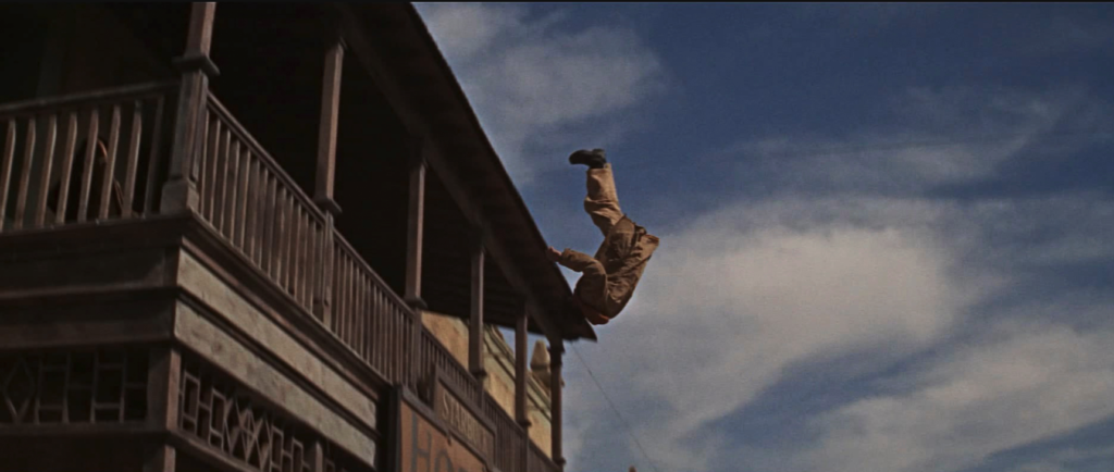 A man gets shot off a balcony as he tumbles through the sky. 
