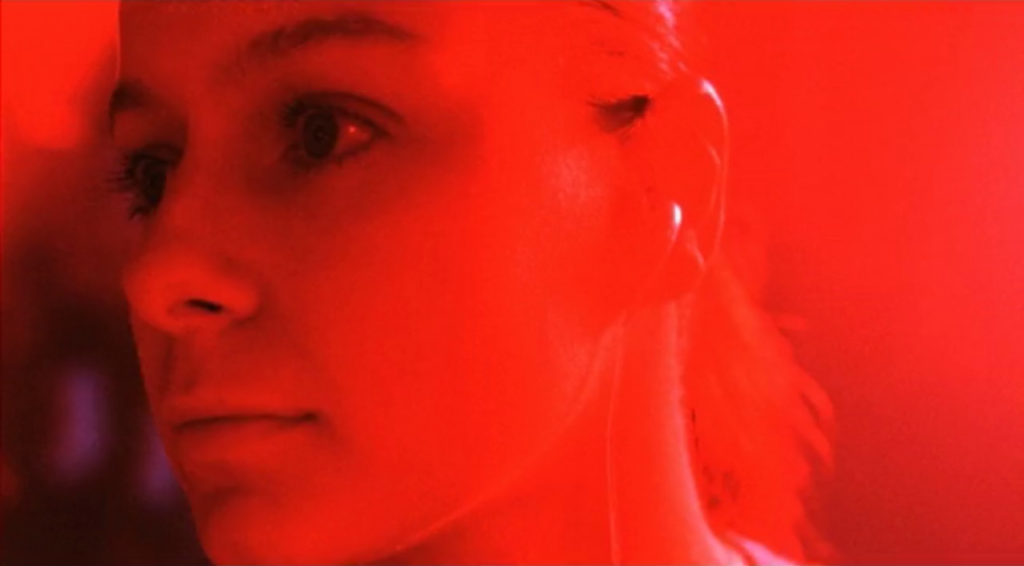 Samantha Morton as Morvern Callar in an extreme close-up in a nightclub. Her face is bathed in red light as she looks off-camera.