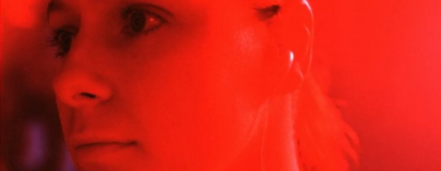 Samantha Morton as Morvern Callar in an extreme close-up in a nightclub. Her face is bathed in red light as she looks off-camera.