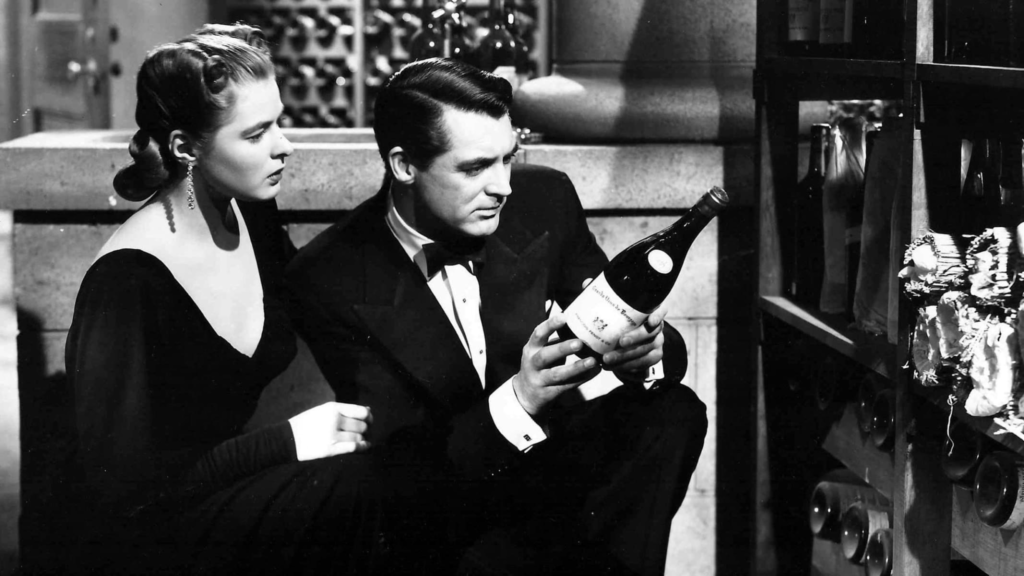 Alicia Huberman, played by Ingrid Bergman, and T.R. Devlin, played by Cary Grant, dressed in an evening gown and tuxedo, respectively, inspect a wine bottle while crouched in a cellar.