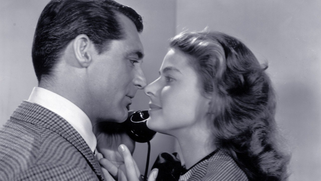 Medium close-up of T.R. Devlin, played by Cary Grant, and Alicia Huberman, played by Ingrid Bergman leaning in for a kiss while Devlin takes a phone call.