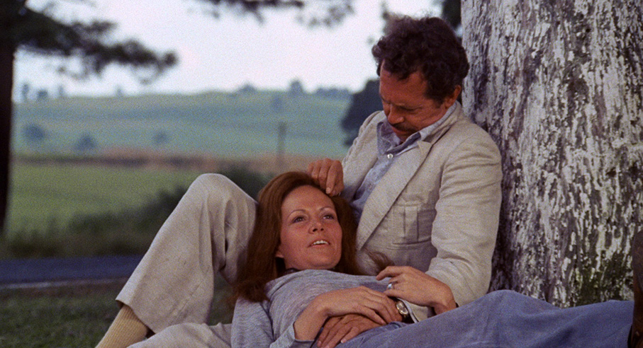 Bennie, white male in beige suit with Elita, red-haired female, lounging in the grass under a tree.