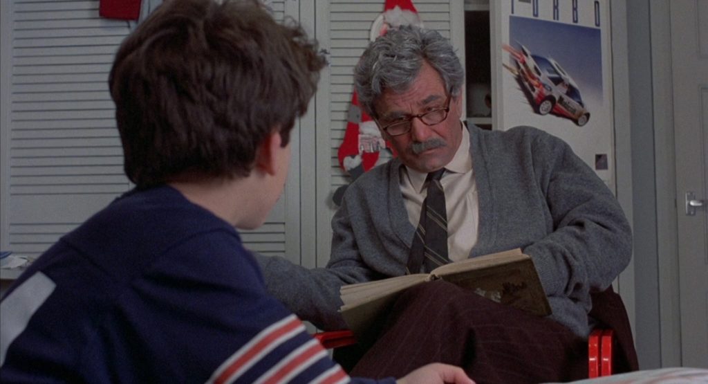 The back of Fred Savage’s head in the foreground facing Peter Falk, who’s looking at him quizzically over the top of his reading glasses.