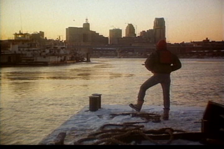 Pulling into St. Paul. (A man stands on a concrete embankment next to the Mississippi River, the city in the background.)