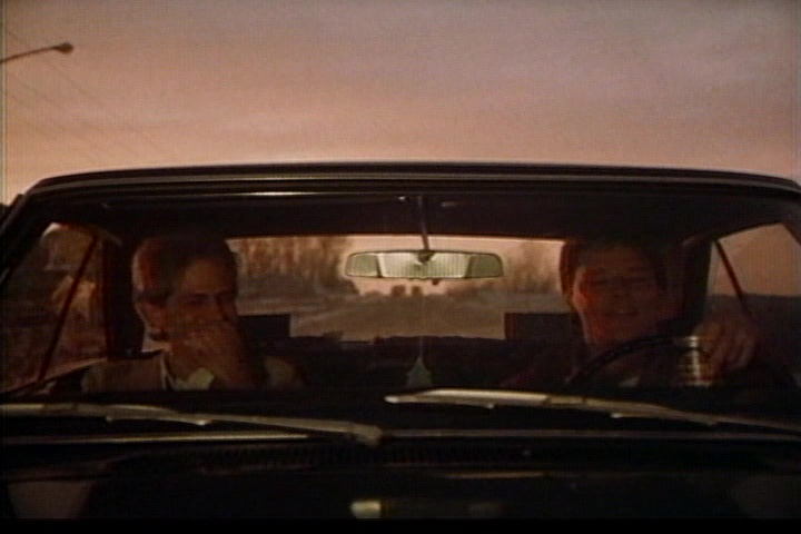 Billy and Eddie in transit (two men speak in a car, the sun in the distance). 