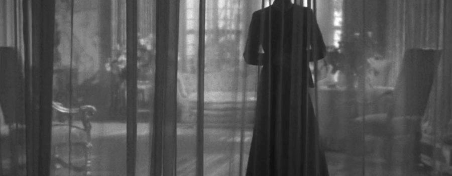 Mrs. Danvers looms in stark silhouette behind a sheer curtain, framed by the lit windows in the background.