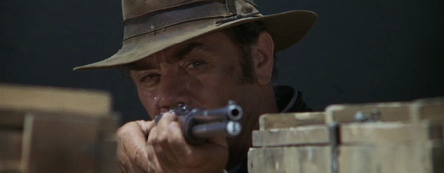 A man in a hat (Ernest Borgnine) stares down the barrel of his rifle in "The Wild Bunch."