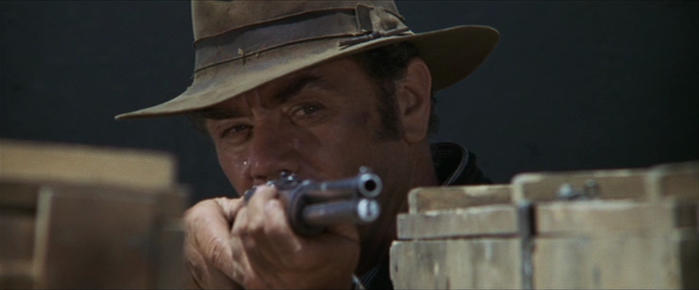 A man in a hat (Ernest Borgnine) stares down the barrel of his rifle in "The Wild Bunch."
