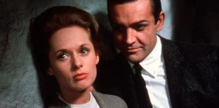 Tippi Hedren leans against a wall, looking offscreen, as Sean Connery stands behind her and looks at her in "Marnie."