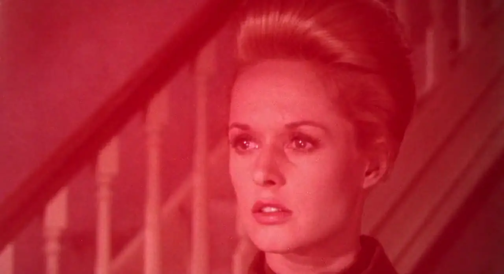 A woman (Tippi Hedren) stares offscreen, bathed in a red filter. 