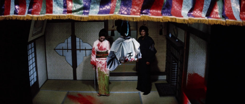 Two images of a blood-splattered Yuki, sword in hand, having just dismembered one of her foes who hangs lifeless from the ceiling before a stage curtain lowers in the foreground.
