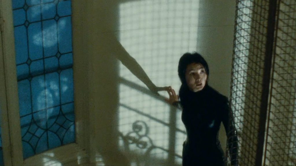 Maggie Cheung ascends a staircase with a grid shadow on the wall behind her in "Irma Vep."