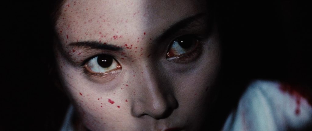 Lady Snowblood (Meiko Kaji) in extreme closeup, her face is flecked with blood, she is looking upward past the camera.