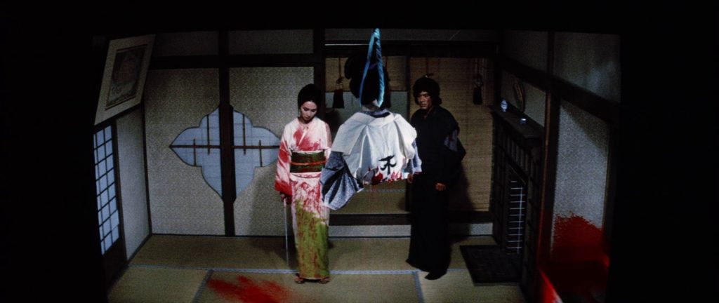 Lady Snowblood (Meiko Kaji) and Ryūrei Ashio (Toshio Kurosawa) look upon a woman hanging by her neck from the ceiling who has been cut in half above the waist.