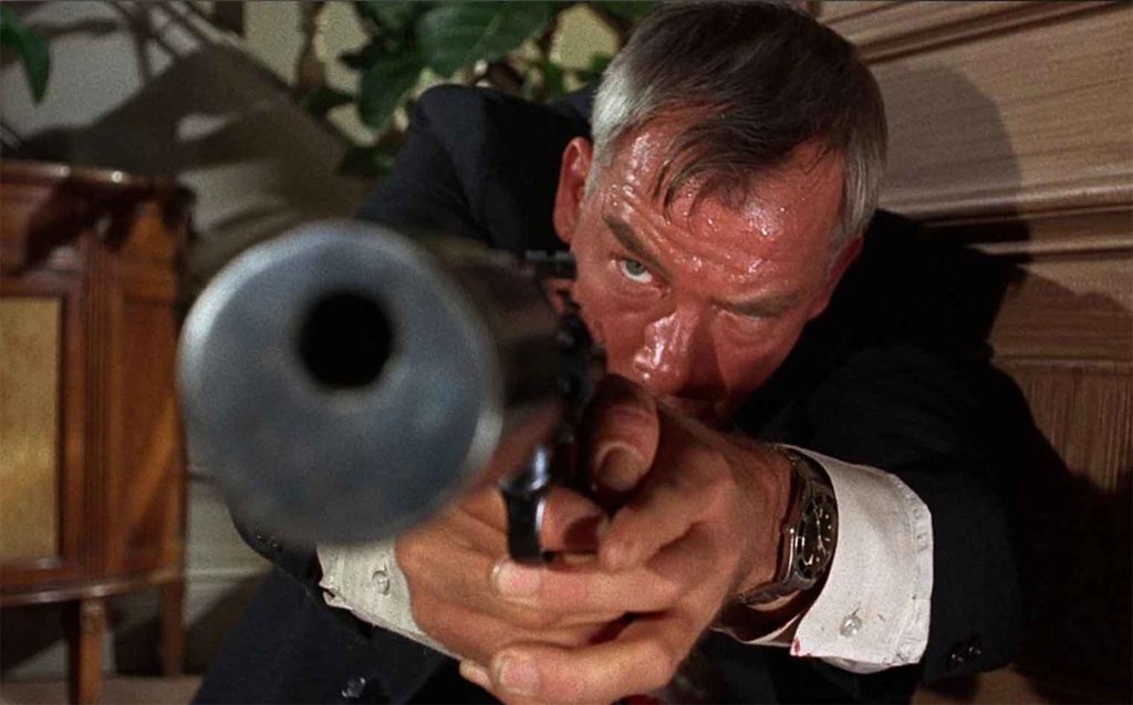A man (Lee Marvin) points a pistol at the viewer in extreme, distorted close-up. 