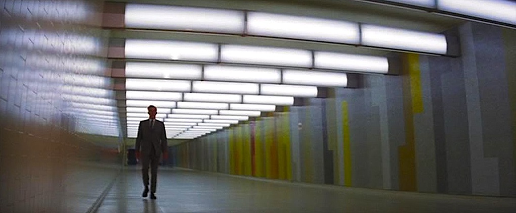 A distant Walker approaches through a stark, fluorescent lit hallway.