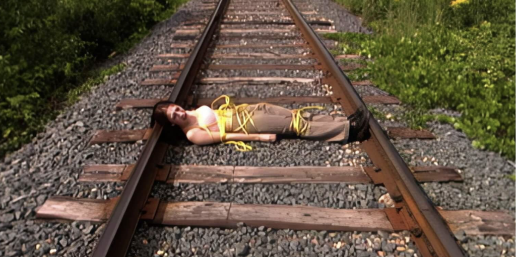 A young woman is lying tied up in yellow rope on train tracks.