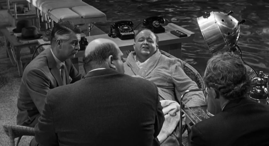 Four men sit in front of a pool. Two of them are facing away from the camera, a third is looking at the fourth, who is a portly man in a robe. 
