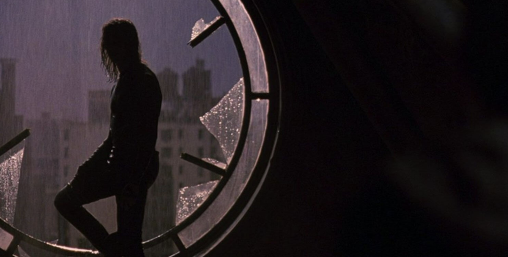 Eric Draven (Lee) stands in a broken window, looking out at a dark city