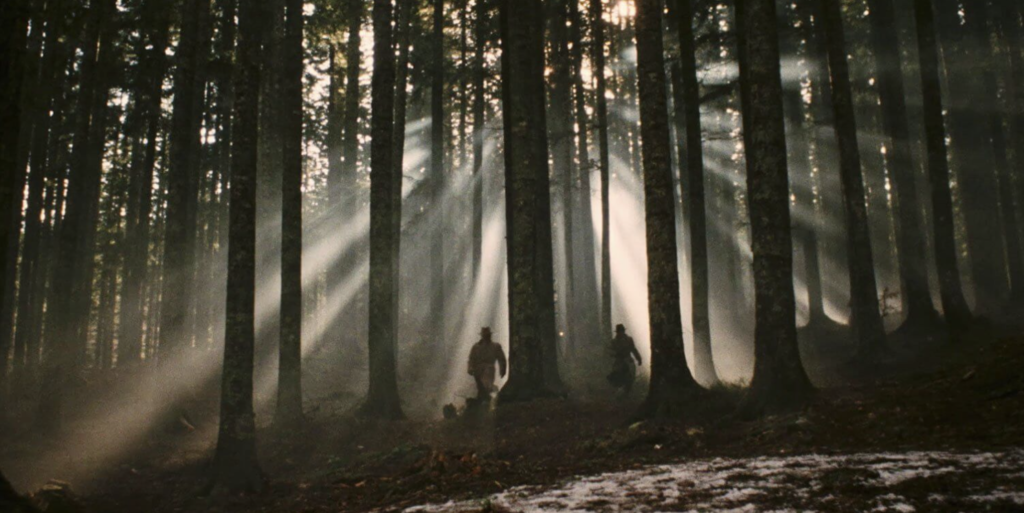 In the dark woods, two men are running to the back of the image.