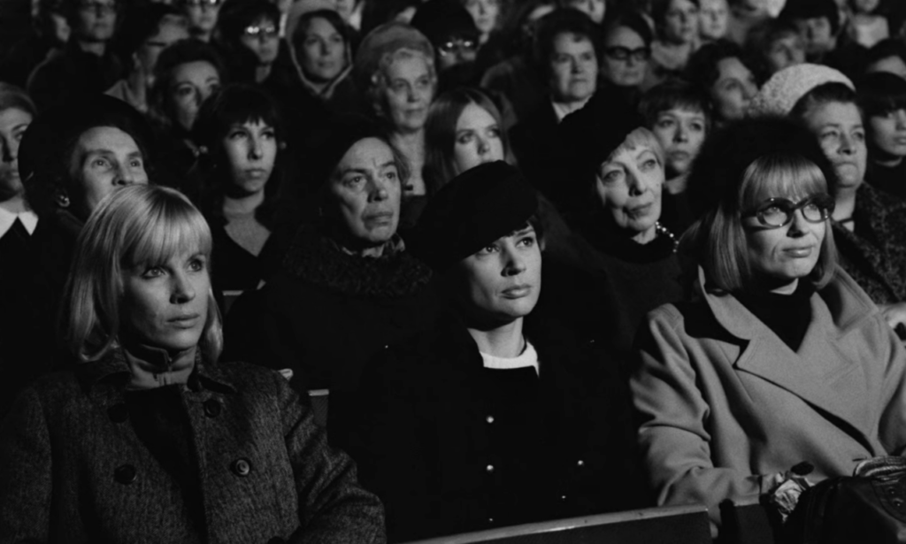 Several rows of a movie theater filled with women, with three white women in the front row as the focal point.