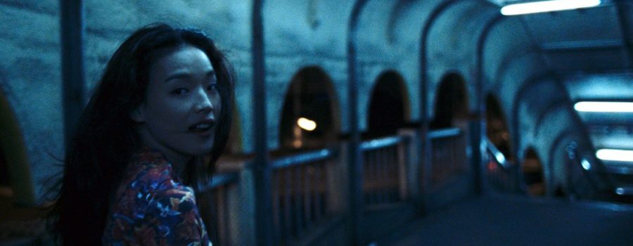 A woman named Vicky, played by actress Shu Qi, is walking through a pedestrian overpass at night, with the lighting putting a blue hue on her and her surroundings. She is looking back over her shoulder at the camera.