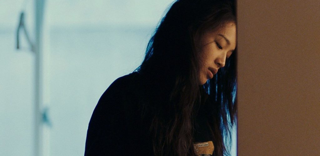 A woman named Vicky, played by actress Shu Qi, stands in an apartment with her head leaning on a wall and with her eyes pointed downward. She has a disaffected look on her face. The background details of the apartment are too out-of-focus to make out.