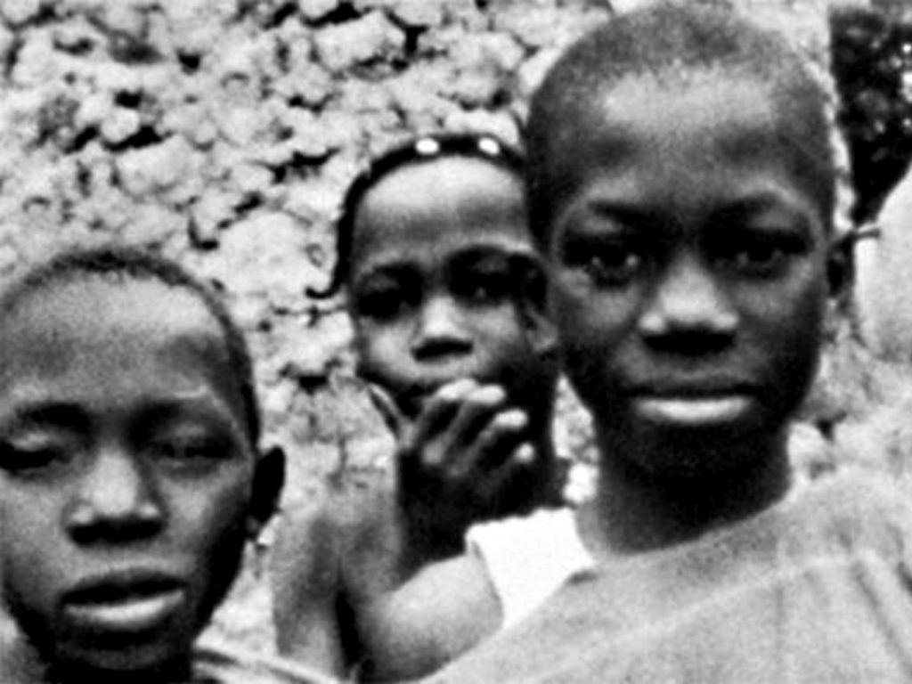 Three African children stare towards the lens of the camera, from the film Afrique 50. 