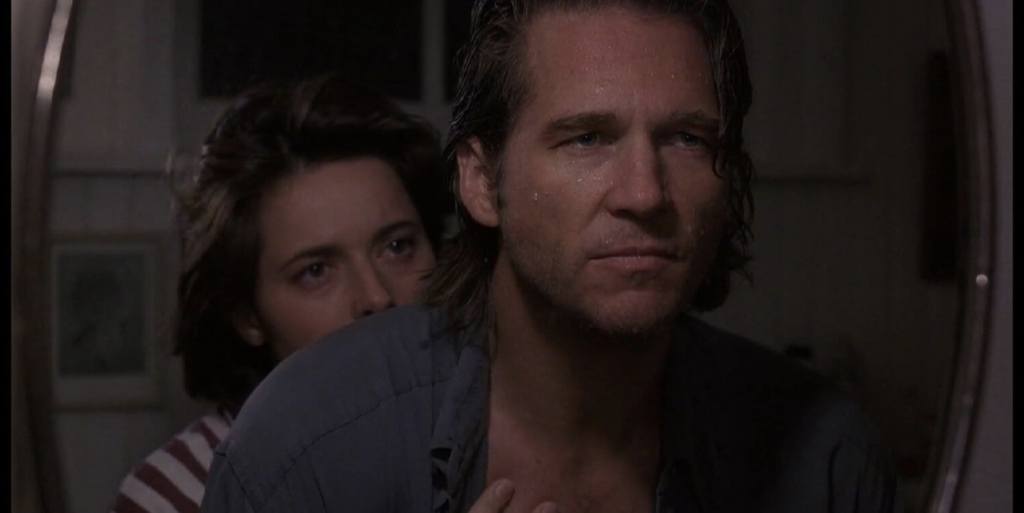 A hot Jeff Bridges glistens with sweat as he stares out a window. Isabella Rossellini pokes her head out from behind his shoulder.