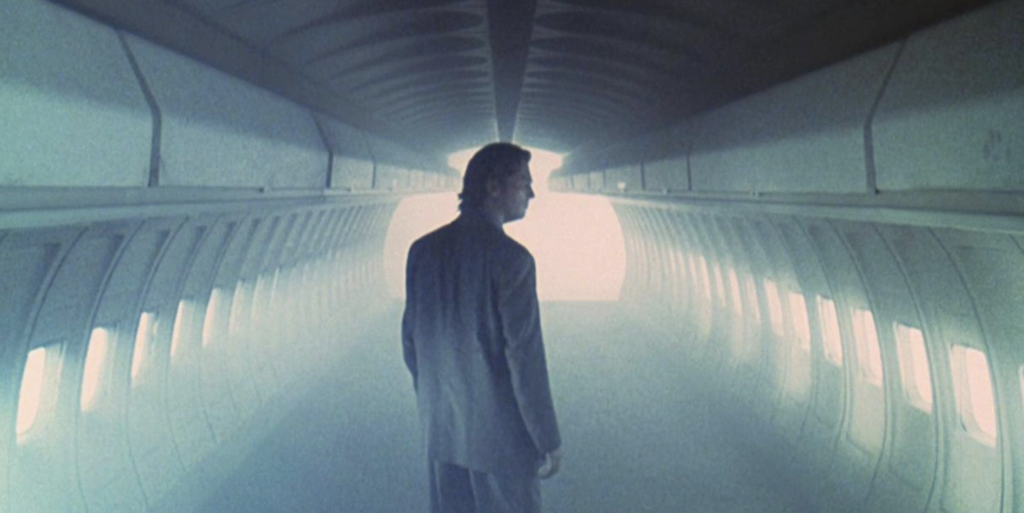 Jeff Bridges stands alone in a misty, blue-lit airplane.